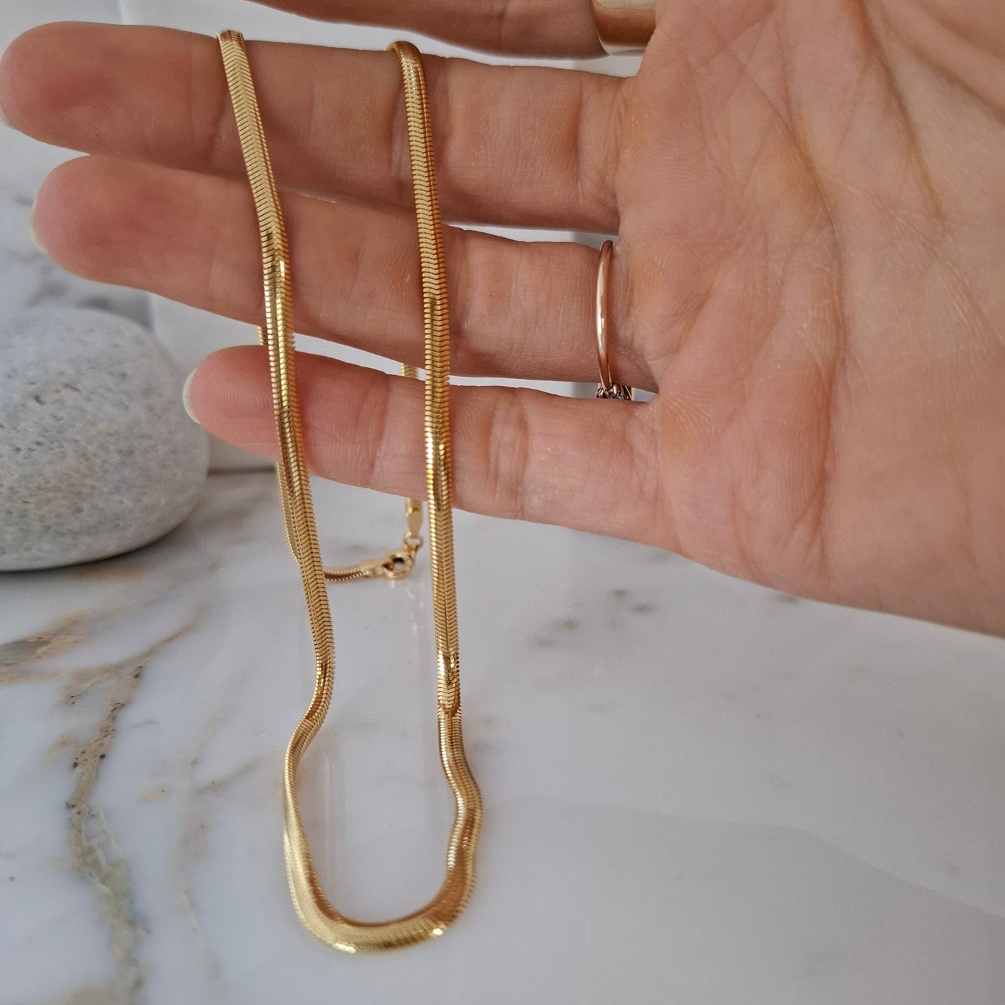 Gold necklace being held in a hand on a marble surface