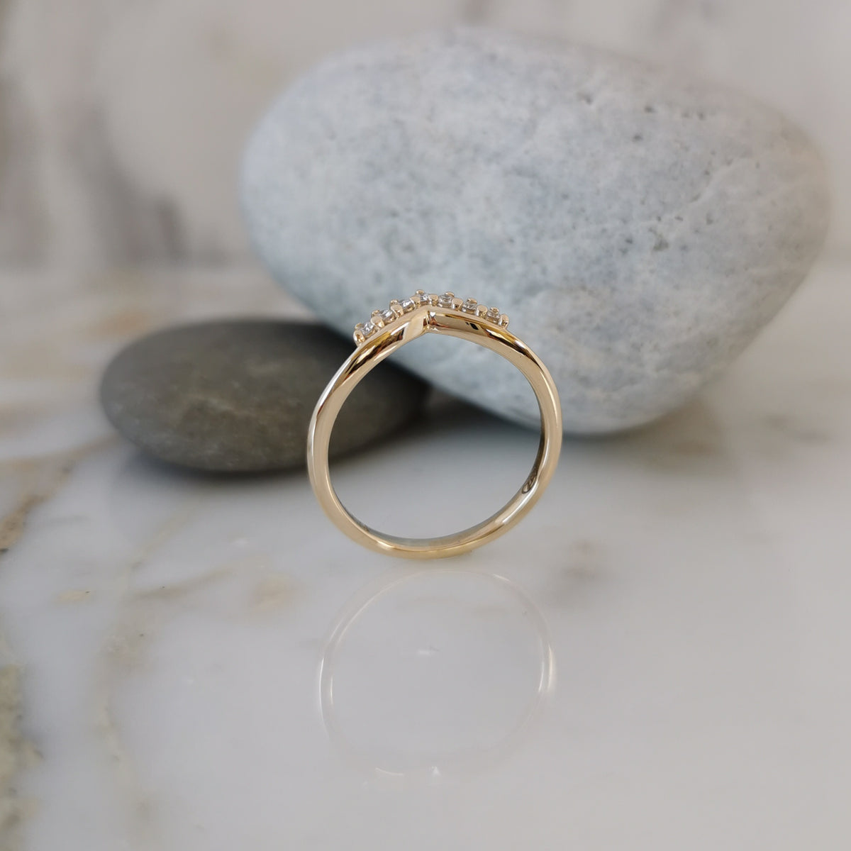 A gold ring with a small cluster of clear stones on the band, displayed on a white marble surface with smooth gray stones in the background.